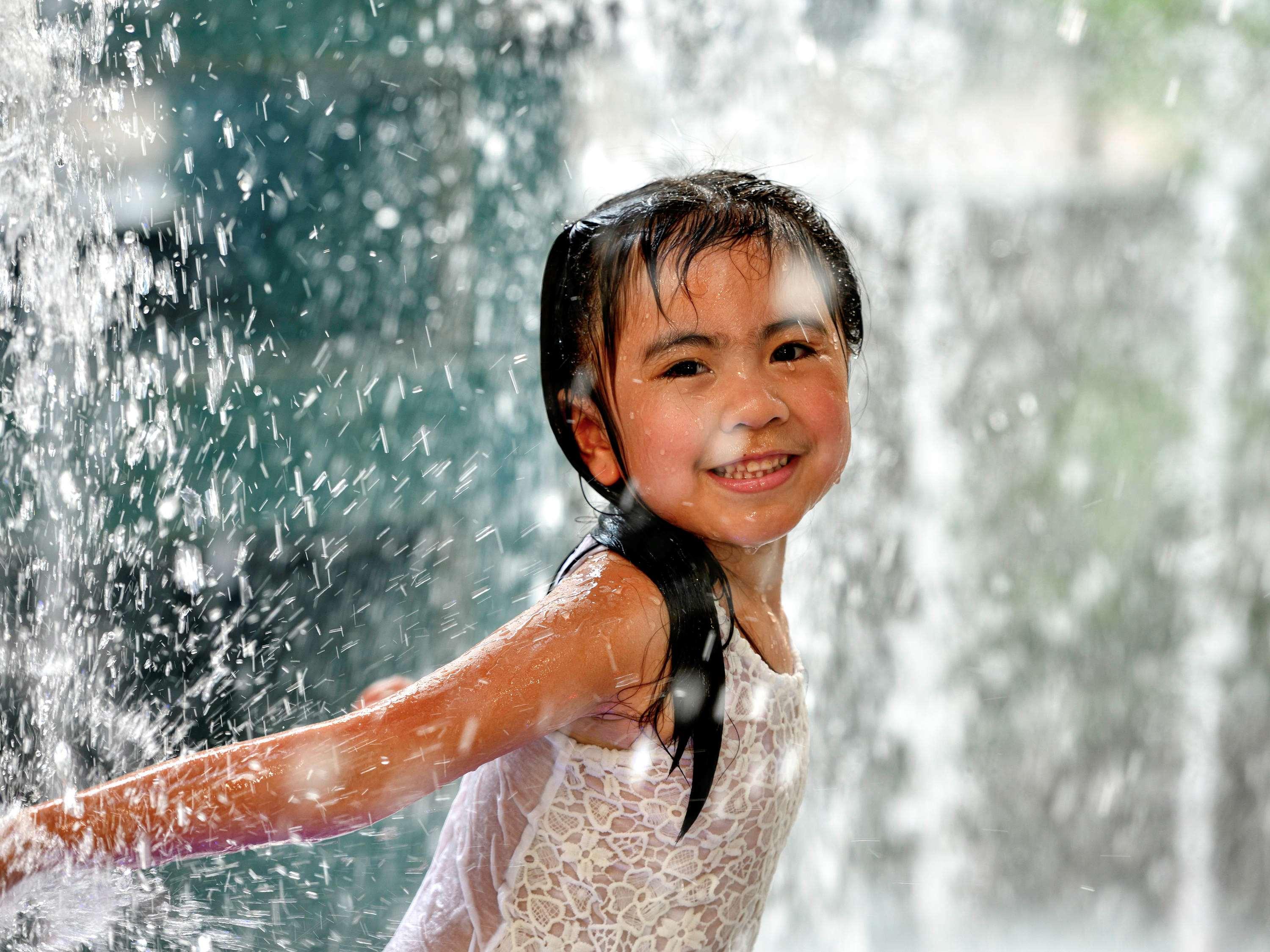 Grand Mercure Dubai City Екстериор снимка The photo shows a young girl joyfully playing in a water fountain. She has wet hair and is wearing a light-colored outfit, possibly a dress or swimsuit. The background features splashes of water cascading down, creating a refreshing and playful atmos